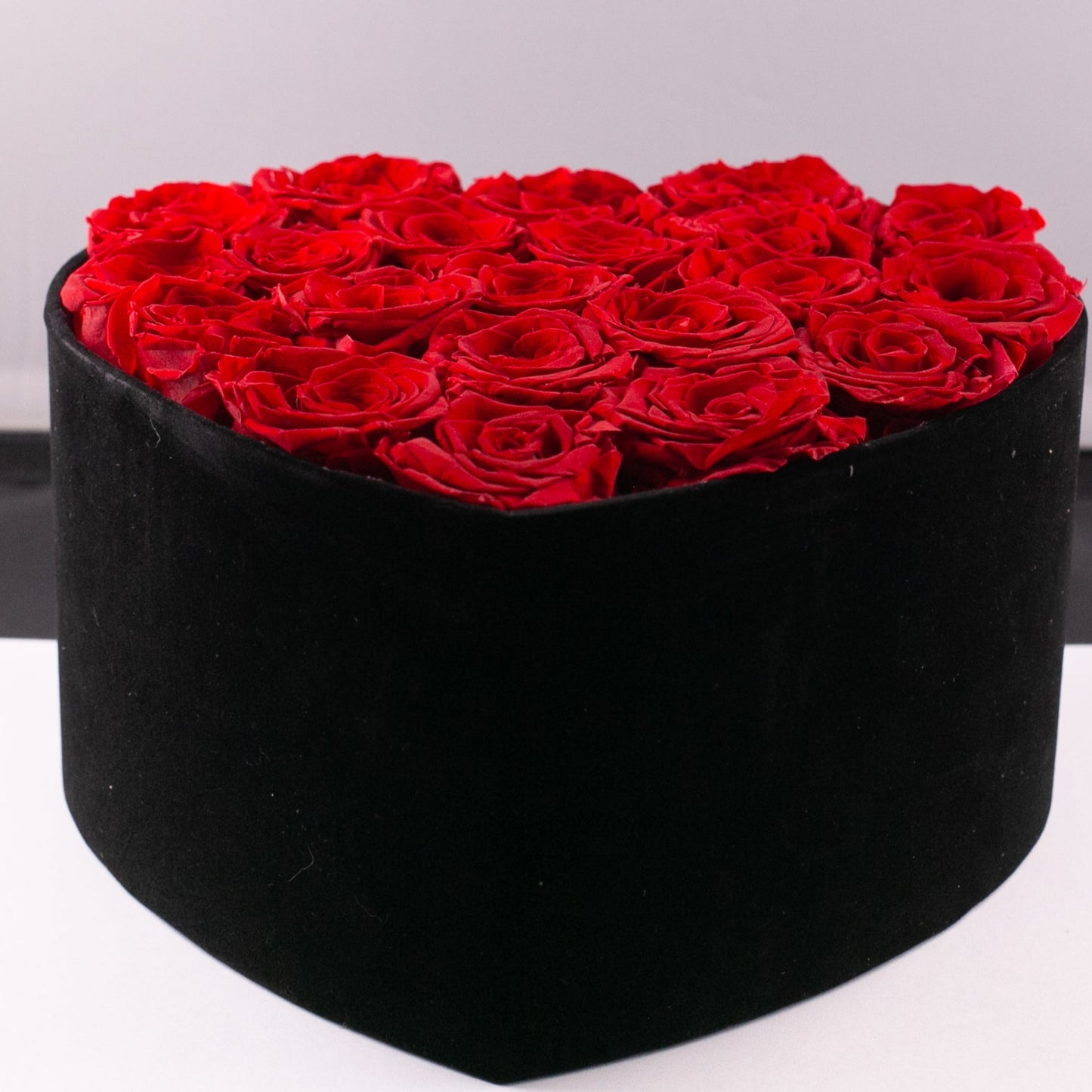 Black heart-shaped box filled with red roses on a white background