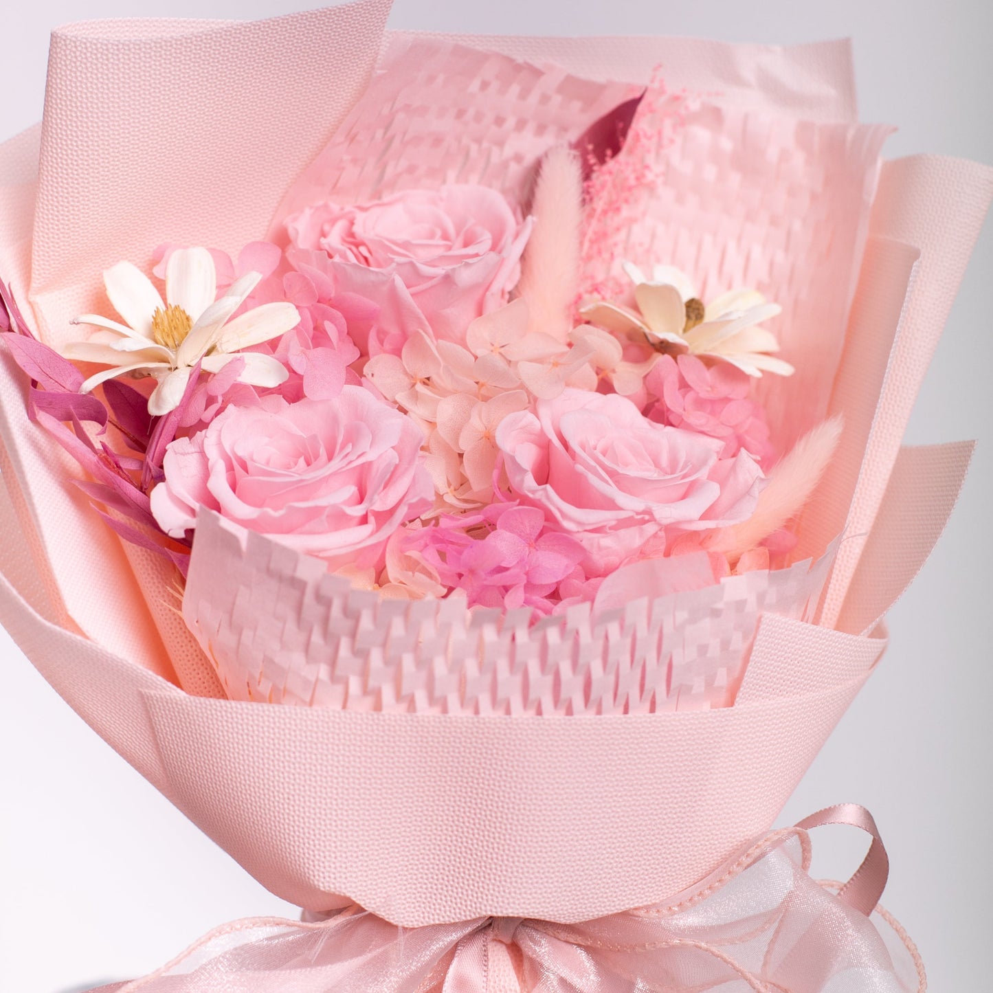Bouquet of pink roses and sola flowers wrapped in pink plastic wrapper with a bow.