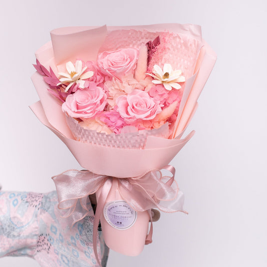 Bouquet of pink roses and sola flowers wrapped in pink plastic wrapper with a bow.