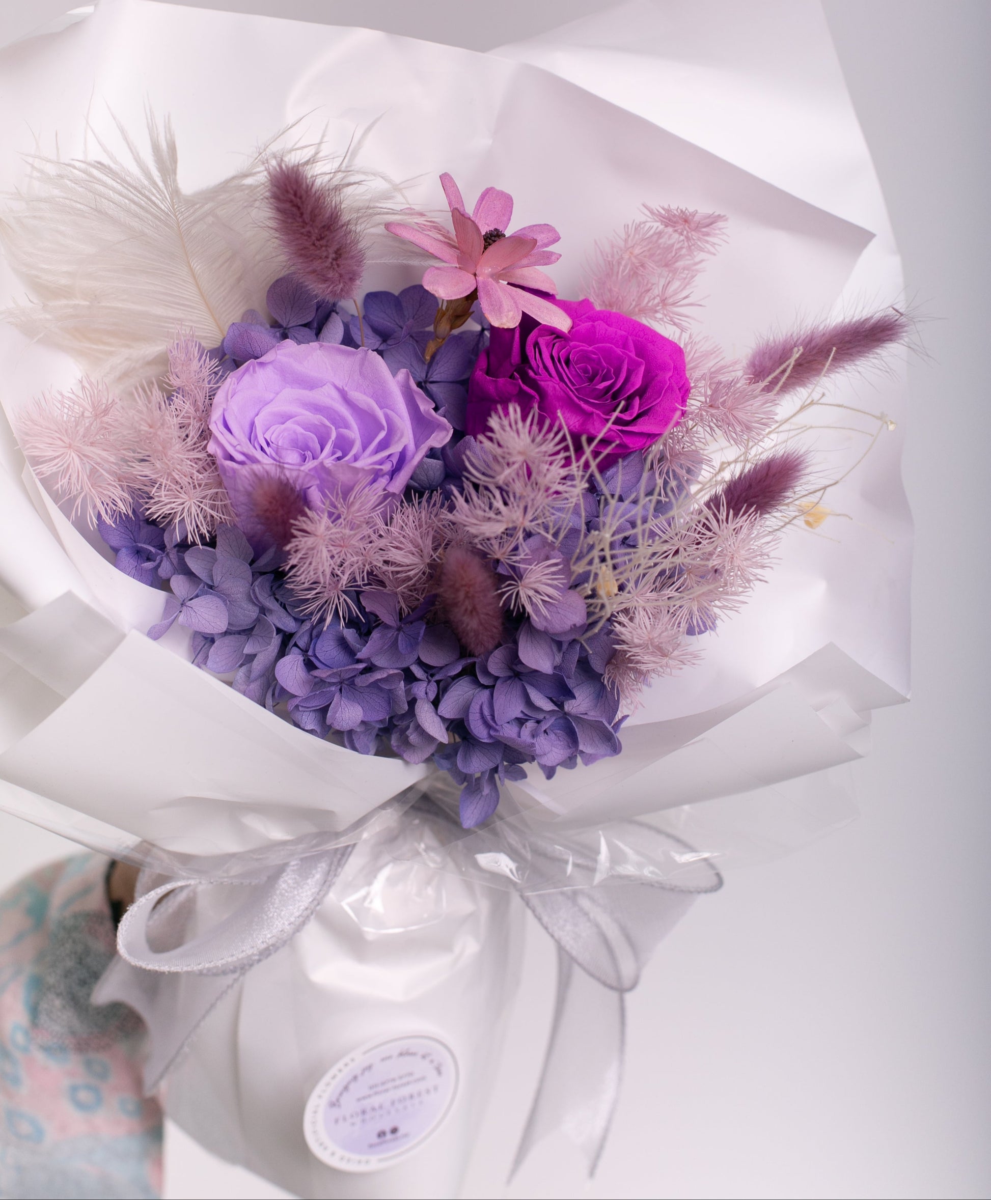 Bouquet of roses, hydrangeas and sola flowers wrapped in white paper with a visible brand label on a white background